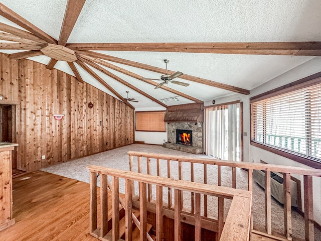 230 Tanglewood Dr, Blue Ridge, GA 30513 - unfurnished living room with vaulted ceiling with beams, wood walls, a stone fireplace, a textured ceiling, and a ceiling fan
