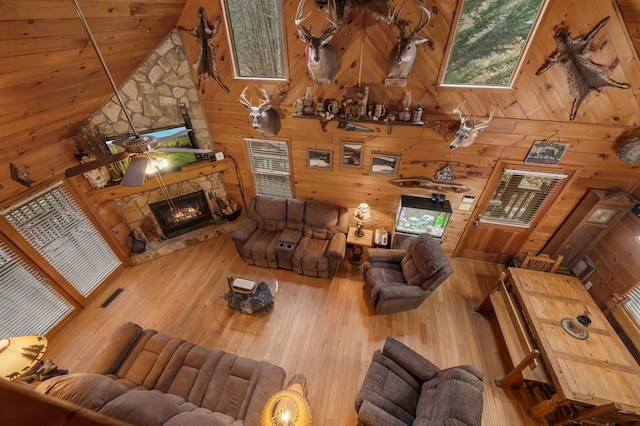 living room with wooden ceiling, high vaulted ceiling, a stone fireplace, wooden walls, and ceiling fan