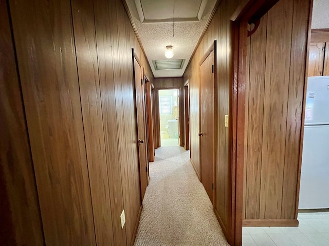 hall with light colored carpet, a textured ceiling, and wooden walls