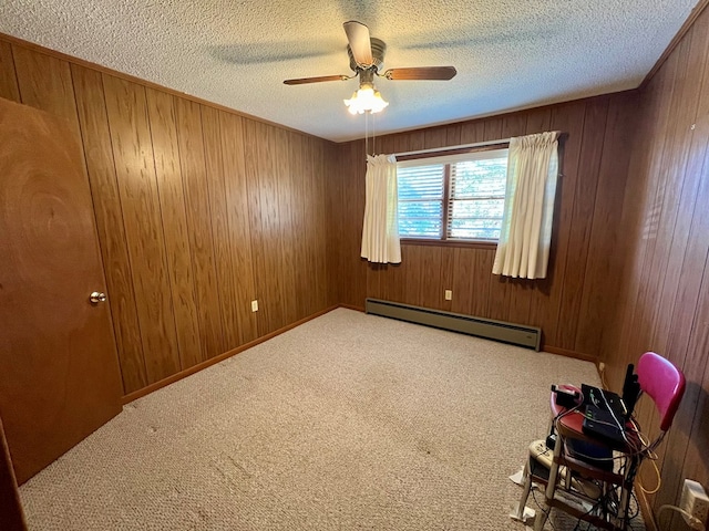 carpeted spare room featuring wood walls, a baseboard heating unit, a textured ceiling, and ceiling fan