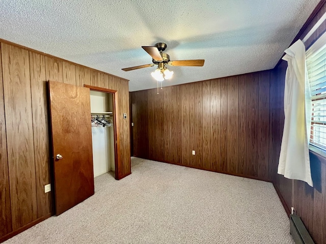 bedroom featuring a closet, a baseboard heating unit, ceiling fan, a textured ceiling, and wood walls