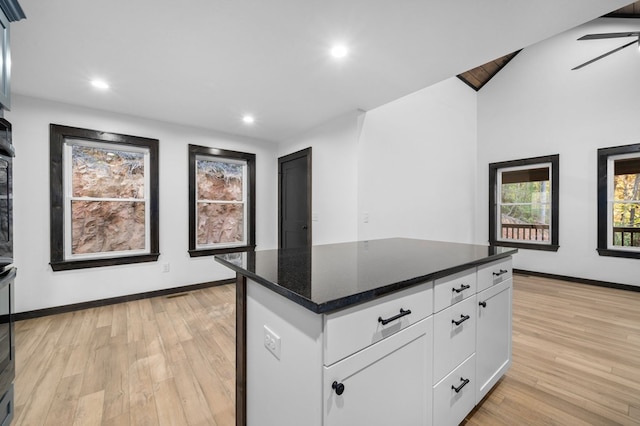 kitchen with lofted ceiling, a kitchen island, white cabinetry, light hardwood / wood-style flooring, and dark stone countertops