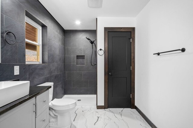 bathroom featuring tile walls, vanity, a tile shower, and toilet