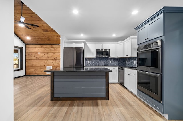 kitchen with lofted ceiling, light wood-type flooring, stainless steel appliances, wooden walls, and a center island