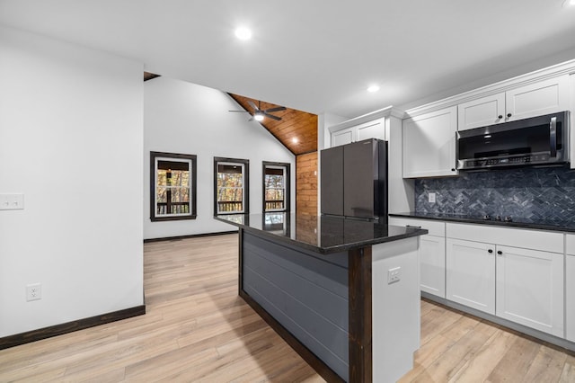 kitchen featuring fridge, a center island, ceiling fan, dark stone counters, and white cabinets