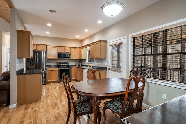 kitchen featuring light wood finished floors, dark countertops, stainless steel appliances, a sink, and recessed lighting