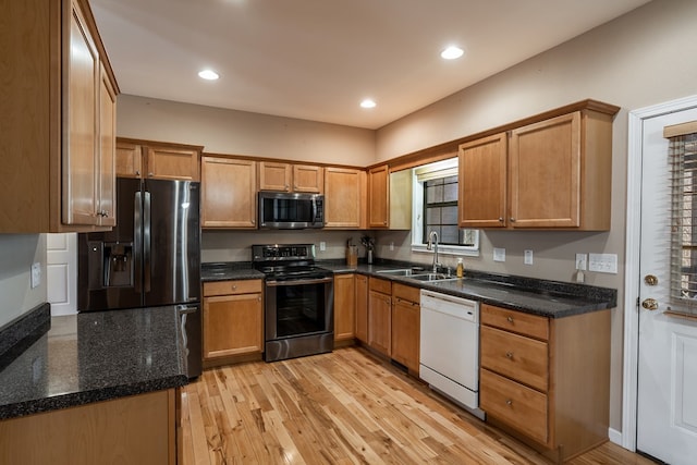 kitchen featuring appliances with stainless steel finishes, brown cabinetry, a sink, and light wood-style flooring