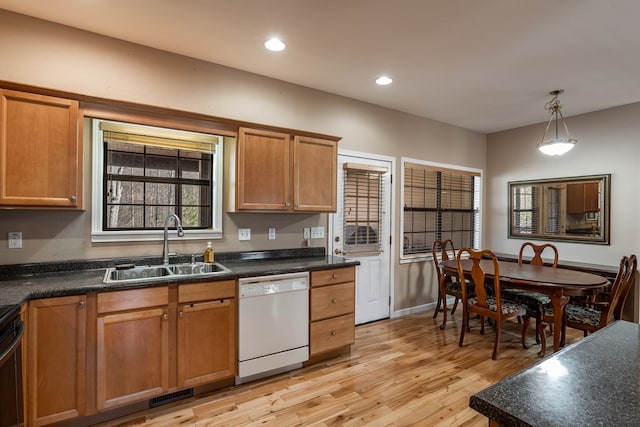 kitchen featuring light wood-style floors, dark countertops, dishwasher, and a sink