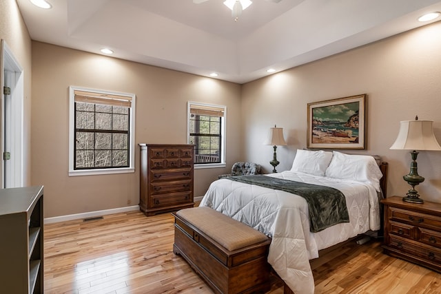 bedroom with light wood-style floors, baseboards, a tray ceiling, and recessed lighting