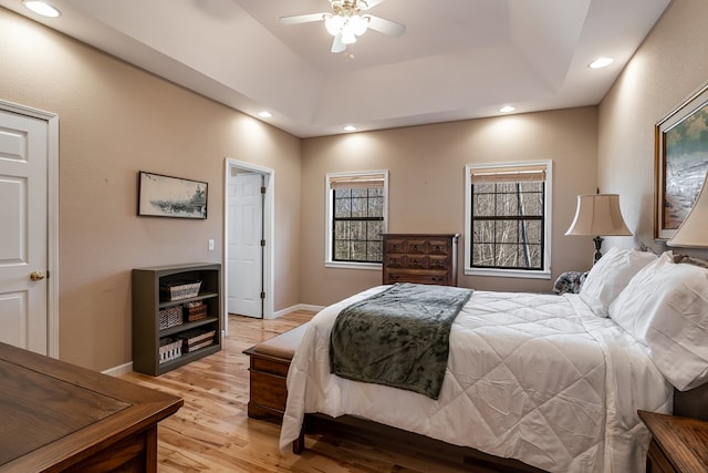 bedroom featuring light wood-type flooring, baseboards, a raised ceiling, and recessed lighting