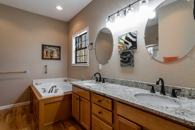 full bath featuring double vanity, a garden tub, a sink, and wood finished floors