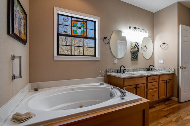 full bath with double vanity, a sink, a tub with jets, and wood finished floors