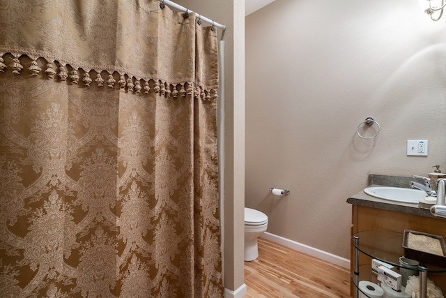 bathroom with toilet, a shower with shower curtain, wood finished floors, vanity, and baseboards