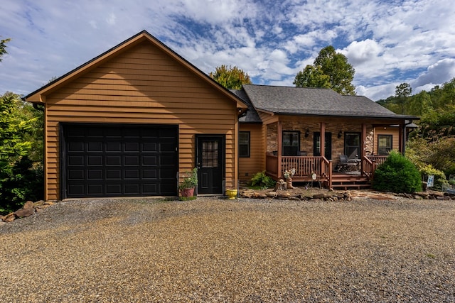 view of front of house with a shingled roof, covered porch, an attached garage, and gravel driveway