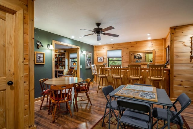 dining area with a dry bar, a ceiling fan, wood finished floors, wood walls, and recessed lighting