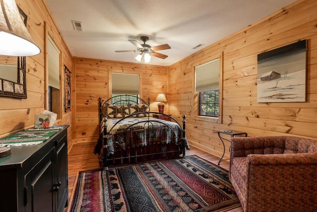 bedroom featuring visible vents, ceiling fan, wooden walls, and wood finished floors