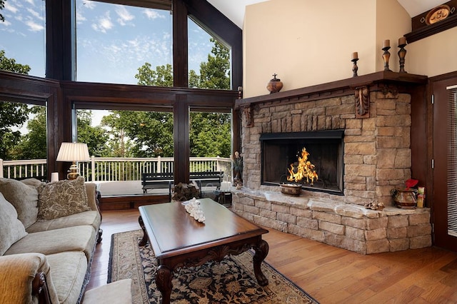 living room featuring wood-type flooring, a towering ceiling, a stone fireplace, and a wealth of natural light