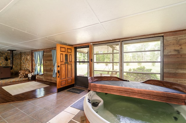 interior space with a wood stove, tile patterned floors, multiple windows, and wooden walls