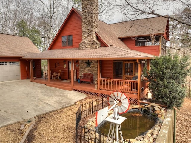 rear view of house featuring a porch, a chimney, an attached garage, and a shingled roof