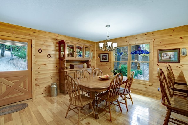 dining space with light wood finished floors, wood walls, and an inviting chandelier