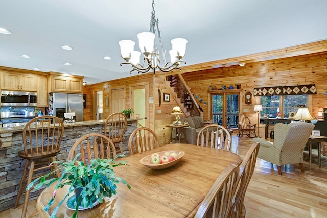 dining area with a chandelier, wood walls, recessed lighting, french doors, and light wood-style floors