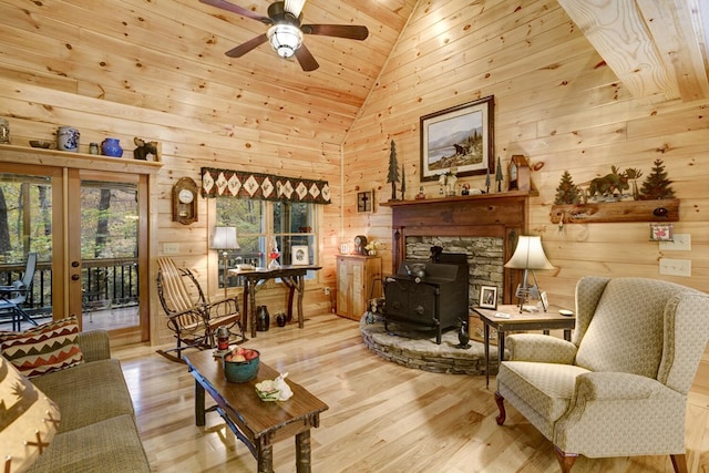 living room with high vaulted ceiling, a ceiling fan, wood finished floors, wood walls, and a wood stove