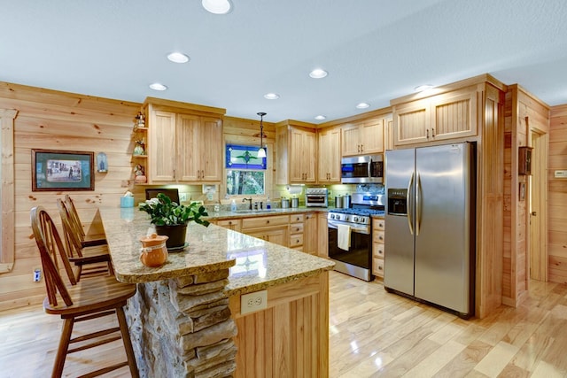 kitchen with light stone counters, a peninsula, a sink, light brown cabinetry, and stainless steel appliances