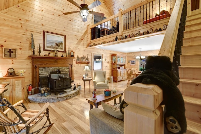 living area with ceiling fan with notable chandelier, wood finished floors, wooden walls, wooden ceiling, and a wood stove