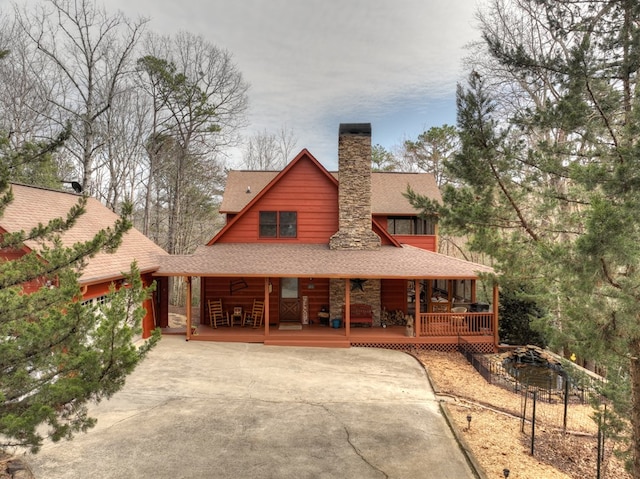 chalet / cabin with a porch, concrete driveway, a chimney, and a shingled roof