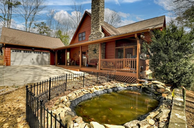 rustic home featuring driveway, a garden pond, fence, an attached garage, and a chimney