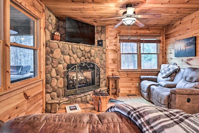 living room featuring hardwood / wood-style flooring, wood walls, a stone fireplace, and wooden ceiling