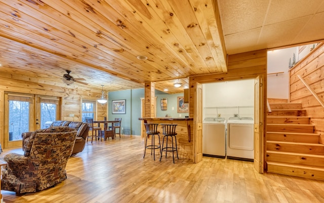 kitchen with washing machine and clothes dryer, a kitchen breakfast bar, wooden walls, and light wood-type flooring