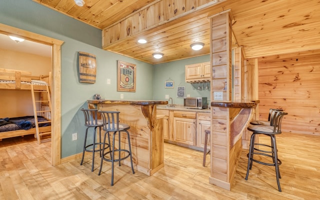 bar with light brown cabinetry, light hardwood / wood-style floors, and wooden ceiling