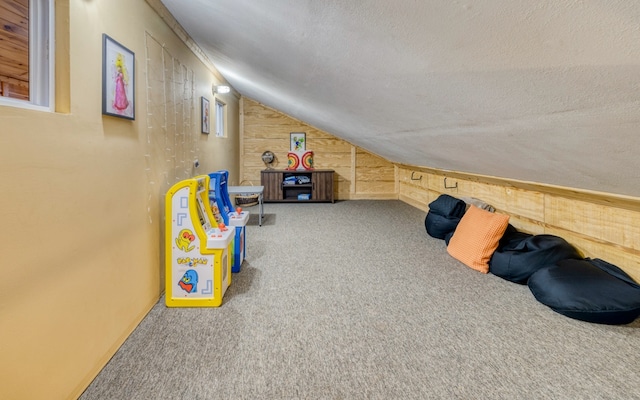 game room with lofted ceiling, light carpet, wood walls, and a textured ceiling