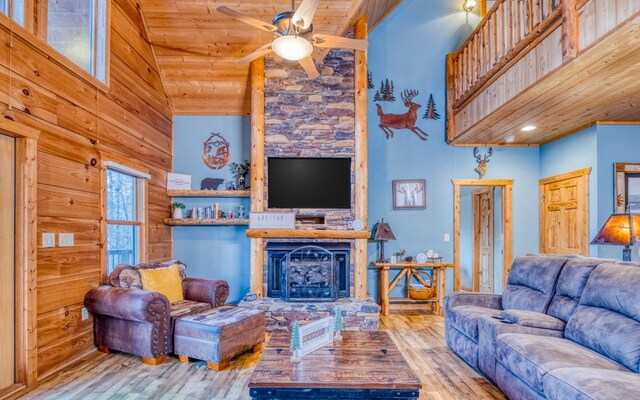 living room featuring ceiling fan, wooden ceiling, high vaulted ceiling, a stone fireplace, and light wood-type flooring