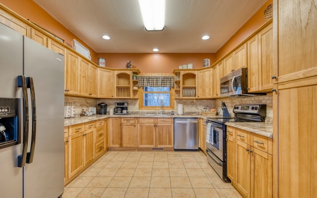 kitchen featuring light brown cabinetry, appliances with stainless steel finishes, backsplash, light tile flooring, and light stone countertops