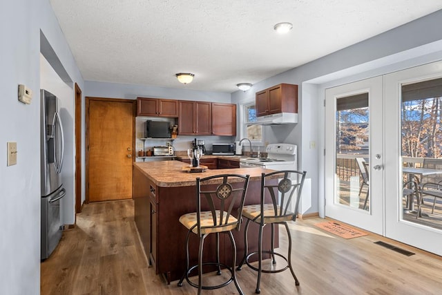 kitchen with stainless steel fridge, wood-type flooring, a textured ceiling, a kitchen island with sink, and a breakfast bar