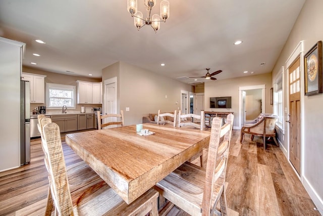 dining space with sink, ceiling fan with notable chandelier, and light wood-type flooring