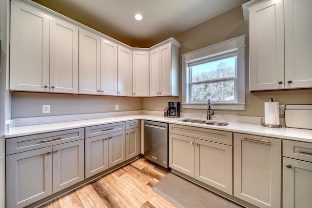 kitchen featuring stainless steel dishwasher, light stone counters, light wood-type flooring, and sink