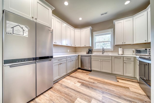 kitchen featuring white cabinetry, sink, light wood-type flooring, and appliances with stainless steel finishes