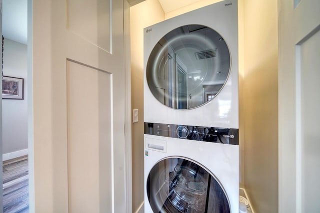 laundry area with stacked washer / dryer and hardwood / wood-style flooring