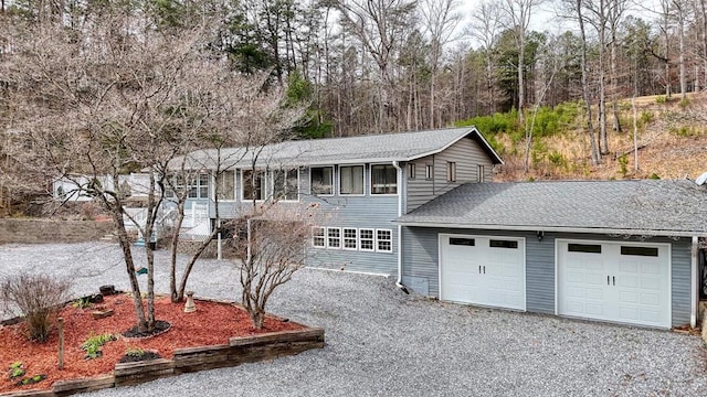 traditional home featuring an attached garage, a shingled roof, and gravel driveway