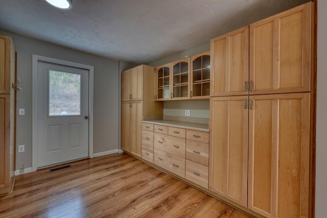 kitchen with light wood finished floors, light brown cabinets, glass insert cabinets, baseboards, and light countertops