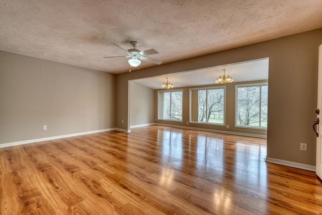 spare room featuring baseboards, a textured ceiling, wood finished floors, and ceiling fan with notable chandelier