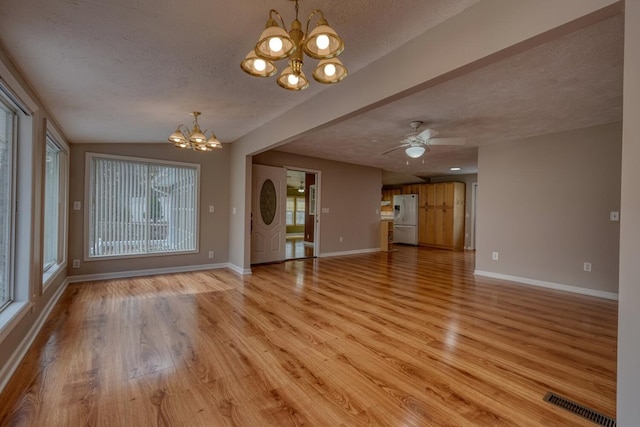 unfurnished living room with light wood-type flooring, visible vents, baseboards, and a textured ceiling