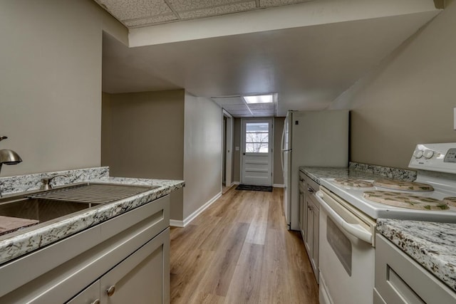 kitchen featuring white appliances, baseboards, light wood-style flooring, a drop ceiling, and a sink