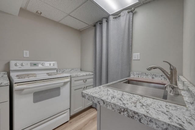 kitchen featuring a drop ceiling, a sink, light countertops, electric stove, and light wood-type flooring