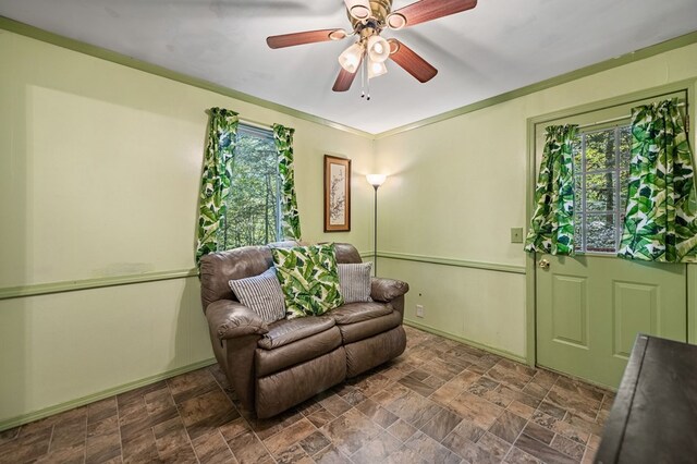 living area with ceiling fan, plenty of natural light, and crown molding