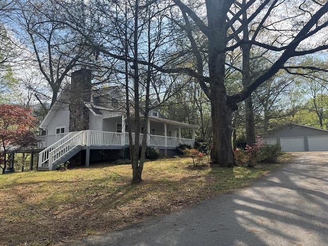 view of side of property featuring an outbuilding, a detached garage, a chimney, covered porch, and stairs
