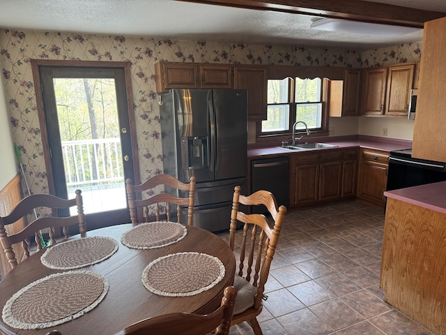 kitchen with a sink, wallpapered walls, a textured ceiling, black appliances, and brown cabinets